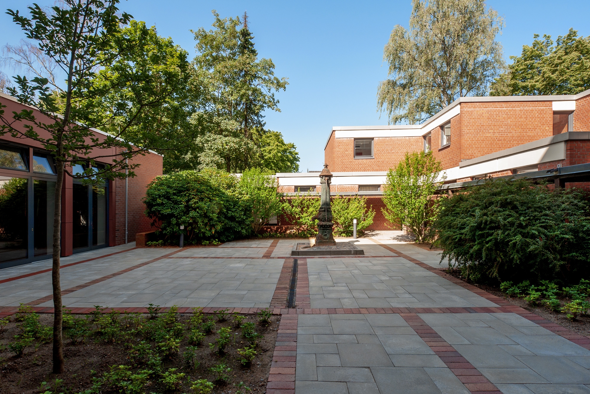 Innenhof mit Büschen, Bäumen und gepflasterem Weg der Wohnanlage Esther-Bejarano-Haus