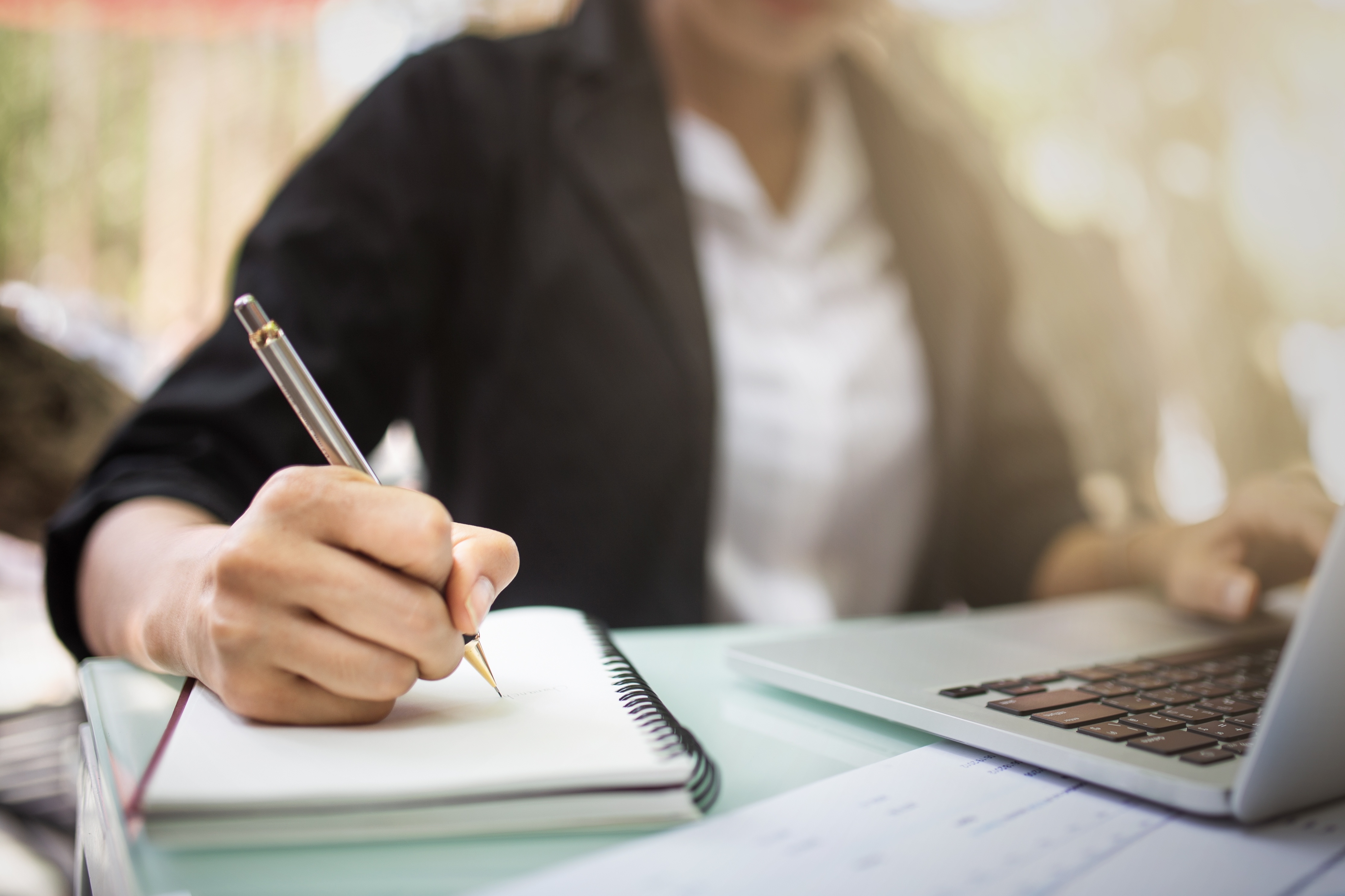 Frau am Schreibtisch schreibt in einen Notizblock Frau am Schreibtisch schreibt in einen Notizblock
