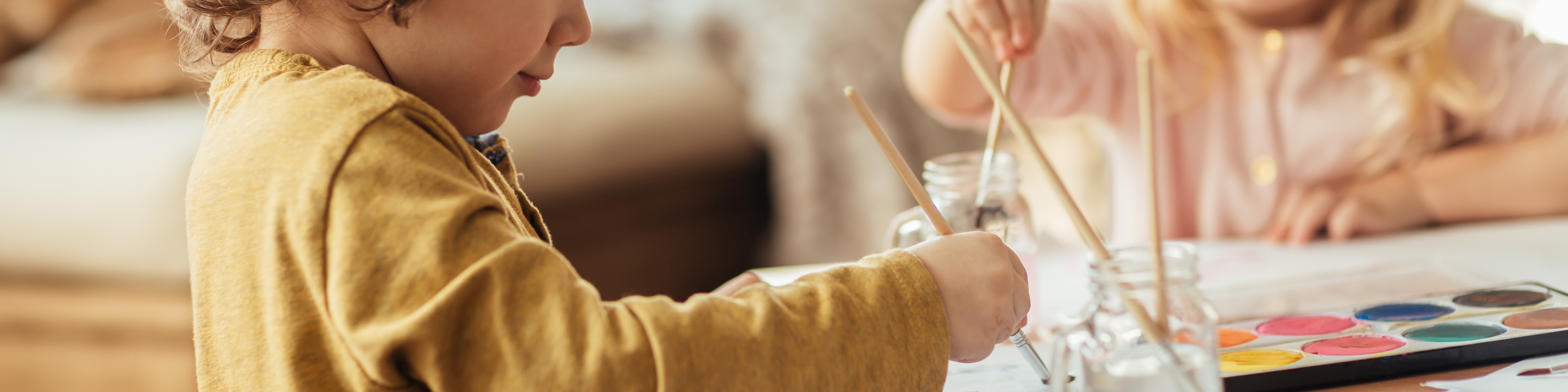 Zwei kleine Kinder sitzen am Tisch und malen mit Farbe und Pinsel