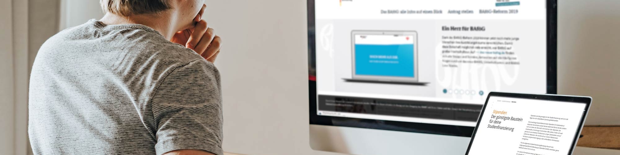 Junger Mann sitzt vor seinem PC und Laptop am Schreibtisch