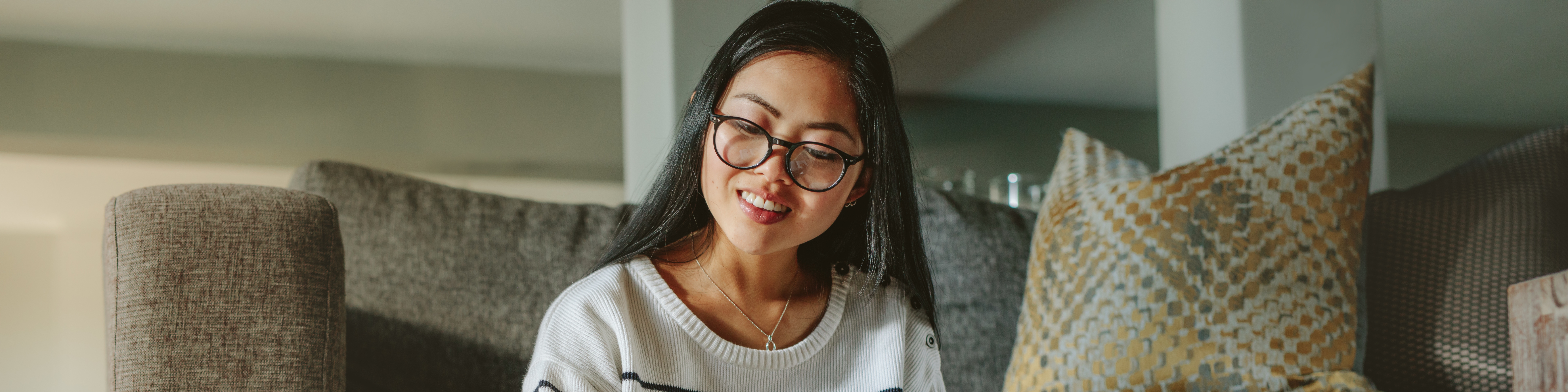 Junge Frau mit Laptop sitzt auf dem Boden angelehnt an ein Sofa 