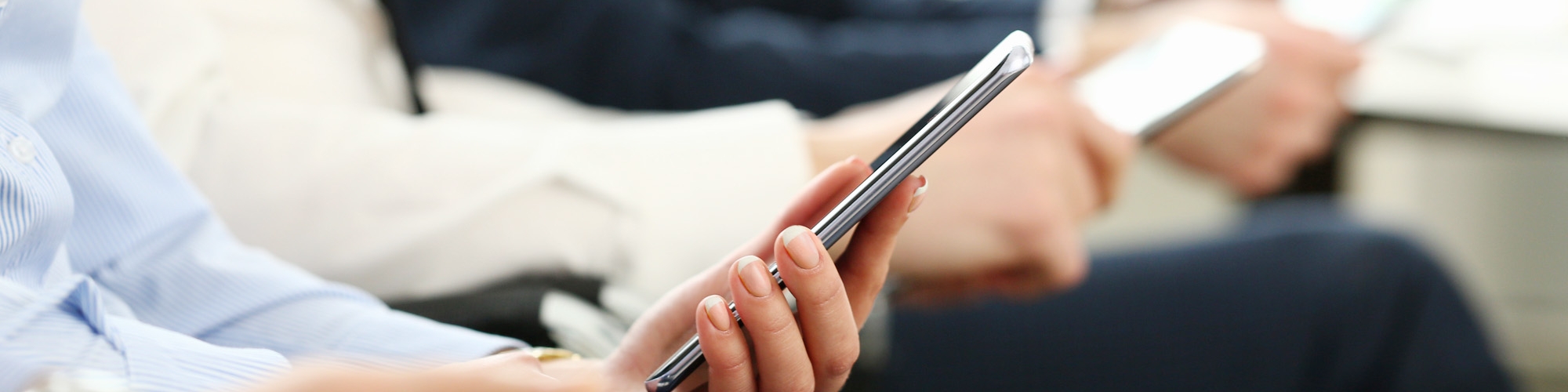 Vier Menschen sitzen mit Smartphone und Tablet nebeneinander